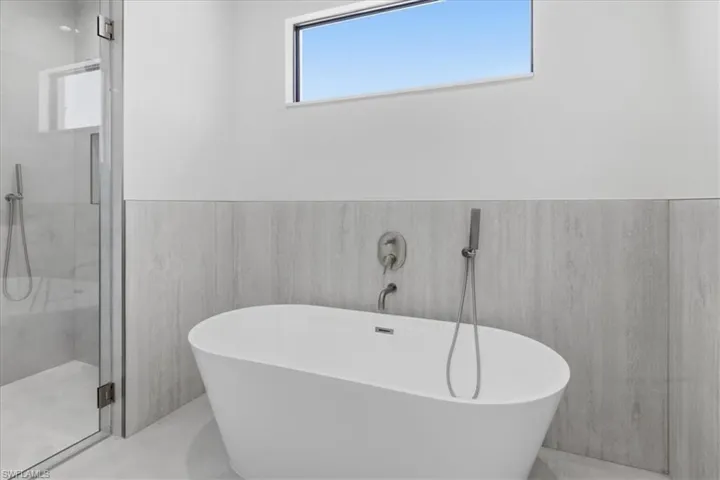 Full bathroom featuring a marble finish shower, wainscoting, a freestanding bath, and tile walls