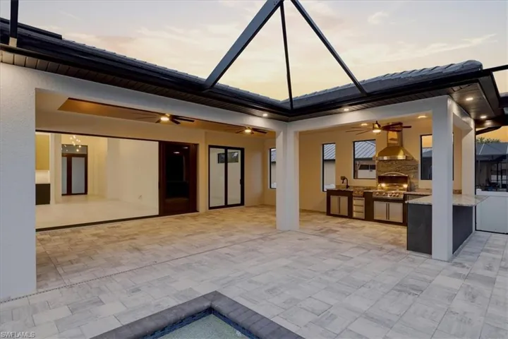 View of patio with an outdoor kitchen, a ceiling fan, and glass enclosure