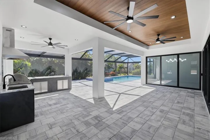 View of patio / terrace featuring an outdoor kitchen, ceiling fan, a sunroom, an outdoor pool, and glass enclosure