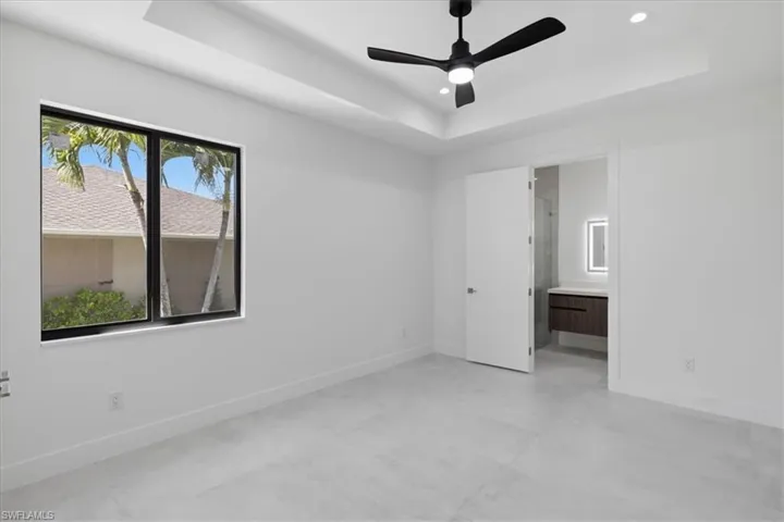 Unfurnished bedroom with finished concrete flooring, ceiling fan, connected bathroom, recessed lighting, and a raised ceiling