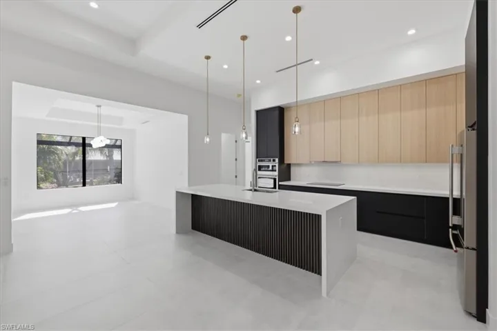 Kitchen with a kitchen island with sink, light stone counters, modern cabinets, stainless steel appliances, and hanging light fixtures