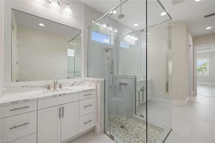 Primary bathroom features dual vanities & frameless shower