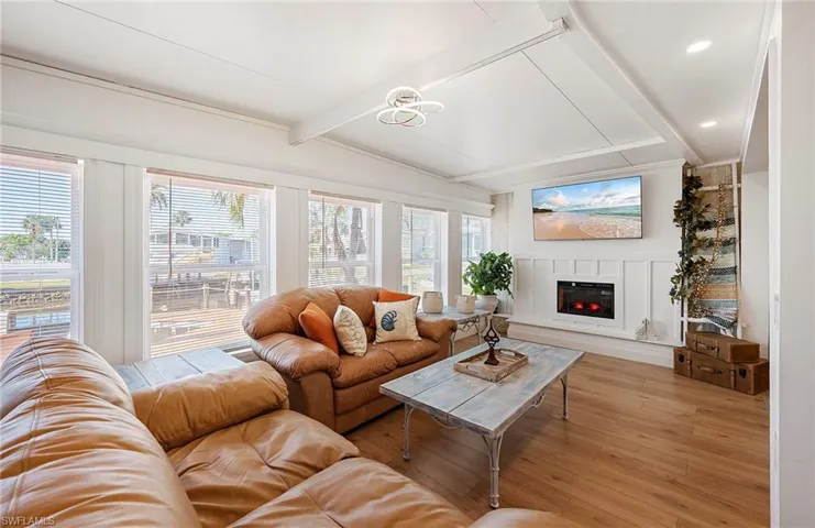 Living room featuring a healthy amount of sunlight, light hardwood / wood-style flooring, and vaulted ceiling with beams