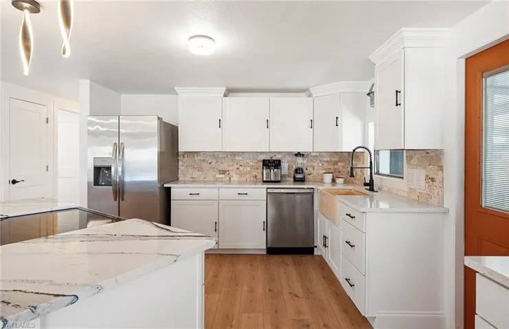 Kitchen featuring white cabinetry, appliances with stainless steel finishes, light stone countertops, and sink