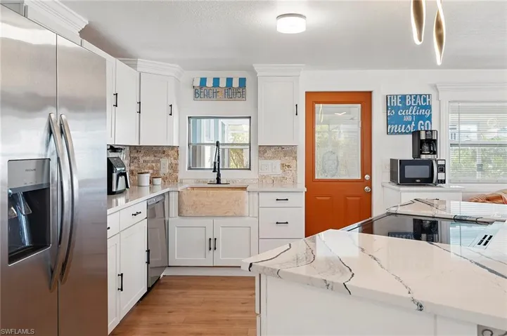 Kitchen with stainless steel appliances, white cabinetry, light stone countertops, and a healthy amount of sunlight