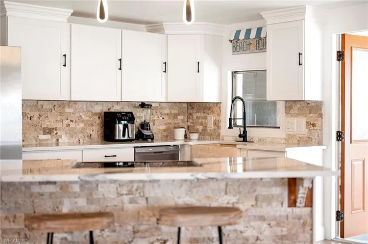 Kitchen featuring tasteful backsplash, white cabinetry, stainless steel dishwasher, and light stone counters