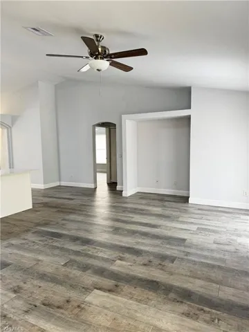 Unfurnished living room with arched walkways, dark wood-style floors, vaulted ceiling, and ceiling fan