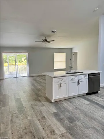 Kitchen featuring white cabinetry, open floor plan, light stone counters, and stainless steel dishwasher