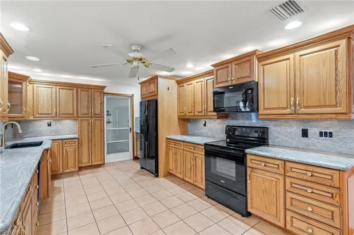 Kitchen featuring backsplash, ceiling fan, black appliances, sink, and light tile floors