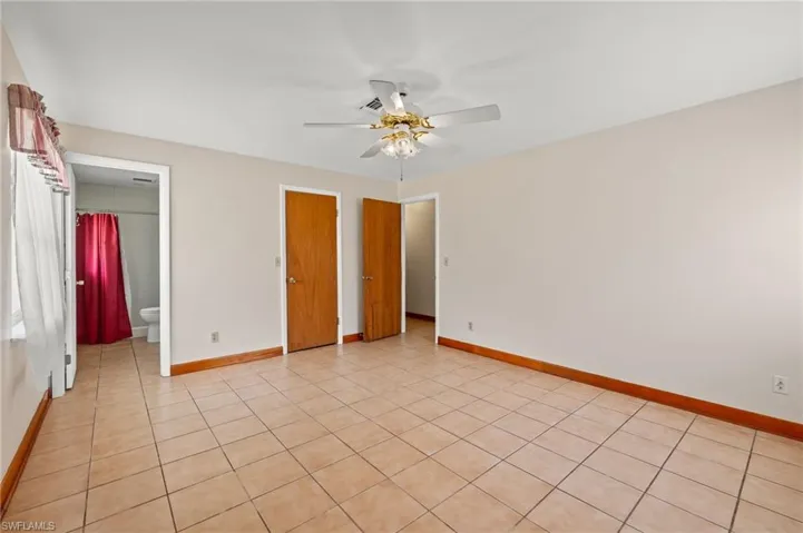 Unfurnished bedroom with connected bathroom, light tile floors, and ceiling fan