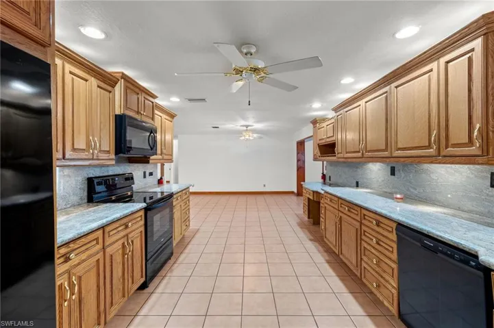 Kitchen with ceiling fan, black appliances, light stone counters, backsplash, and light tile floors