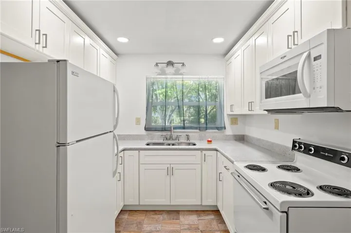 Kitchen featuring white appliances, sink, white cabinetry, and light tile floors
