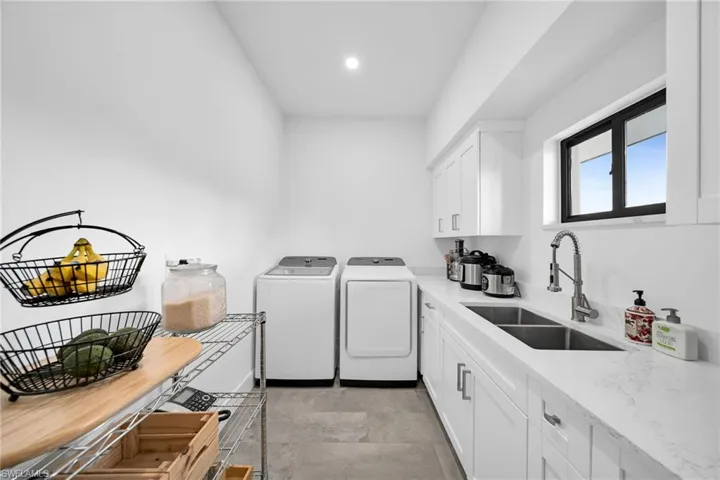 Laundry room featuring sink, washer and clothes dryer, cabinets, and light tile floors