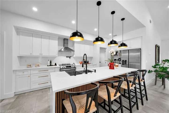 Kitchen with wall chimney range hood, appliances with stainless steel finishes, a kitchen island with sink, decorative light fixtures, and backsplash