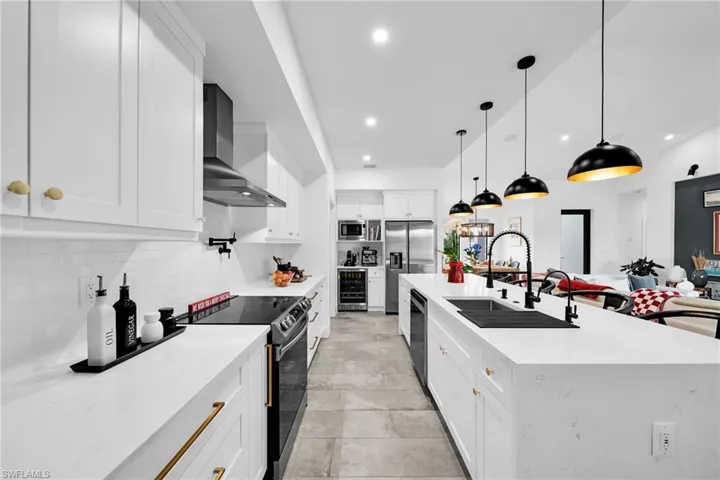 Kitchen featuring tasteful backsplash, decorative light fixtures, wall chimney exhaust hood, white cabinets, and appliances with stainless steel finishes
