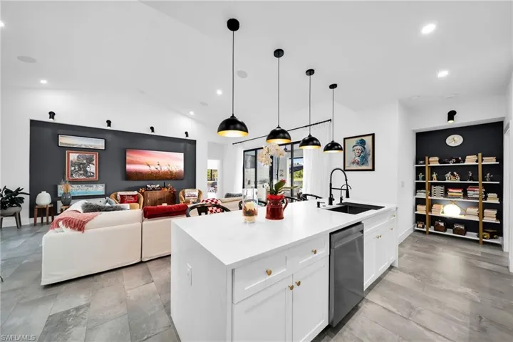 Kitchen featuring vaulted ceiling, dishwasher, a kitchen island with sink, white cabinets, and sink