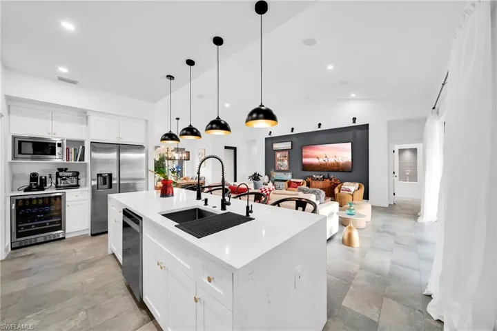 Kitchen with white cabinetry, stainless steel appliances, an island with sink, wine cooler, and pendant lighting