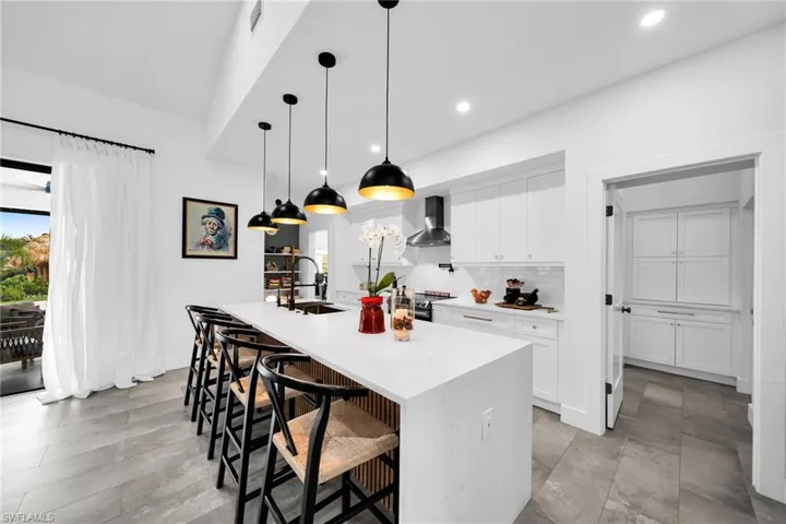 Kitchen with wall chimney range hood, a center island with sink, pendant lighting, a breakfast bar, and sink