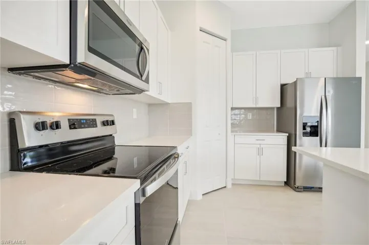 Kitchen featuring appliances with stainless steel finishes, white cabinets, backsplash, and light tile floors