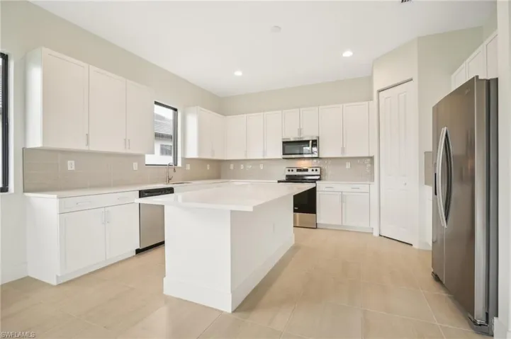 Kitchen featuring tasteful backsplash, light tile flooring, a kitchen island, white cabinets, and appliances with stainless steel finishes