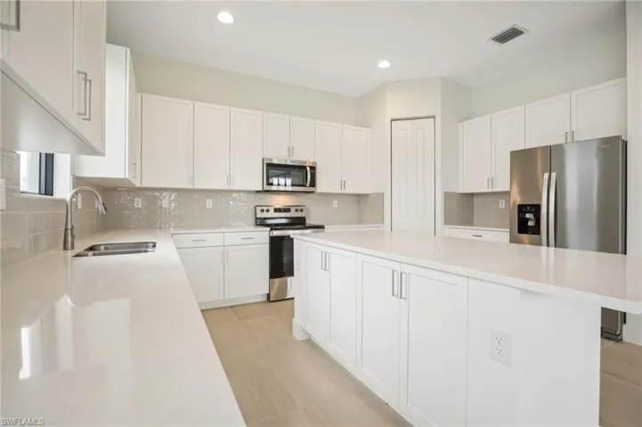 Kitchen with white cabinetry, a kitchen island, stainless steel appliances, sink, and tasteful backsplash