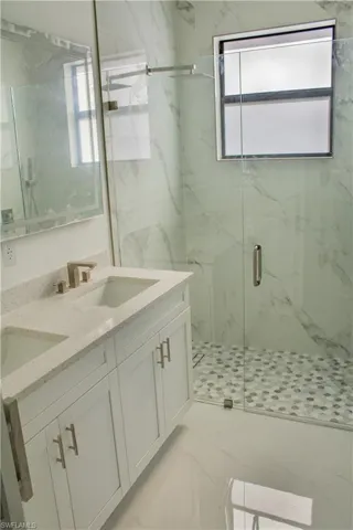 Bathroom with double vanity, a marble finish shower, and light marble finish flooring