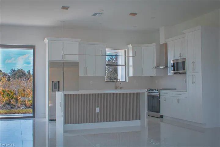 Kitchen with stainless steel appliances, white cabinetry, wall chimney exhaust hood, decorative light fixtures, and a kitchen island
