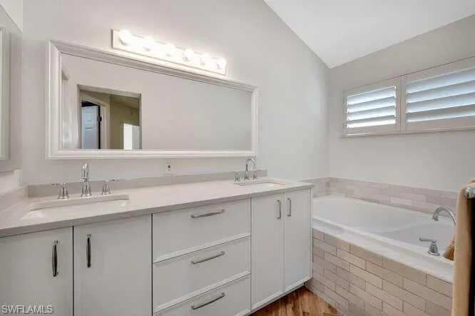 Bathroom with tiled bath, vanity, vaulted ceiling, and hardwood / wood-style flooring