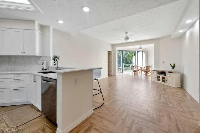 Kitchen with kitchen peninsula, stainless steel dishwasher, ceiling fan, a kitchen bar, and white cabinetry