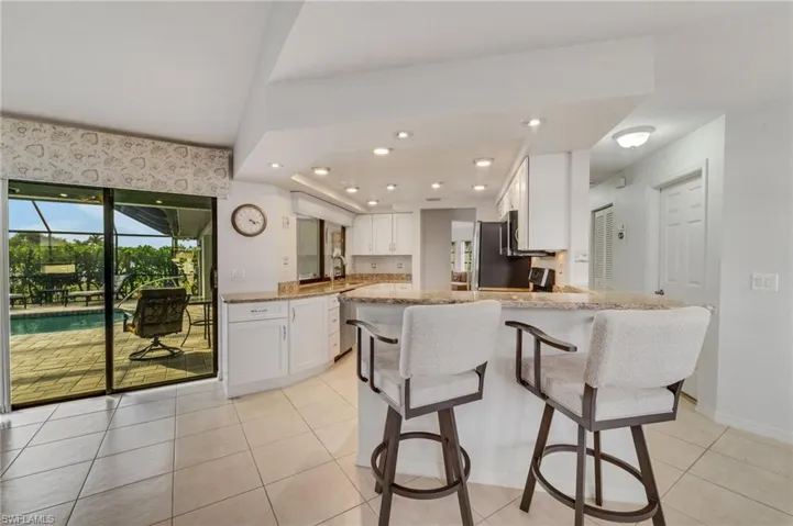 Kitchen featuring light stone countertops, kitchen peninsula, white cabinetry, and light tile floors