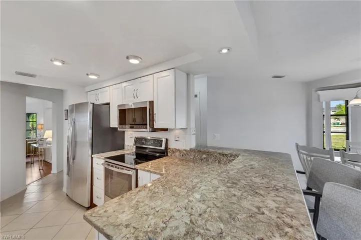 Kitchen featuring white cabinetry, light stone countertops, stainless steel appliances, backsplash, and light tile flooring