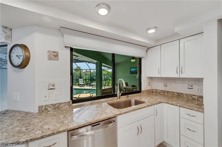 Kitchen featuring white cabinets, light stone counters, dishwasher, tasteful backsplash, and sink