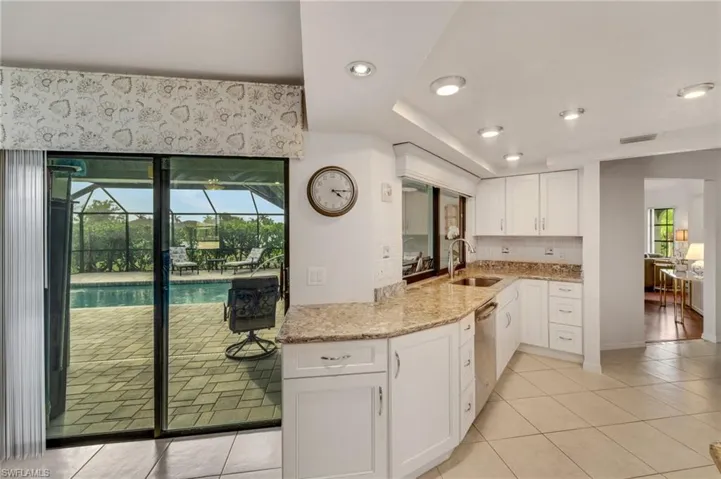 Kitchen with tasteful backsplash, light tile flooring, light stone counters, sink, and white cabinetry