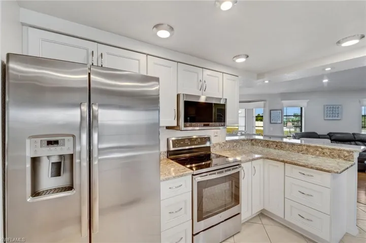 Kitchen featuring light stone countertops, stainless steel appliances, white cabinets, and light tile floors