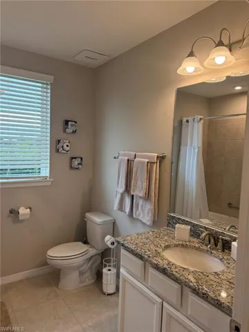 Granite countertop vanity with an undermount sink, ceramic tile flooring, and a shower-tub combination