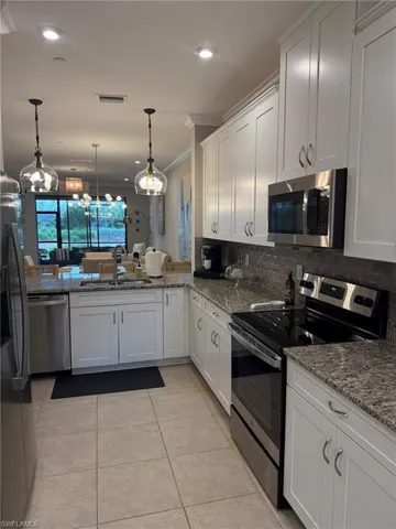 Contemporary kitchen featuring white cabinetry, stainless steel appliances, granite countertops, tile flooring, and pendant lighting