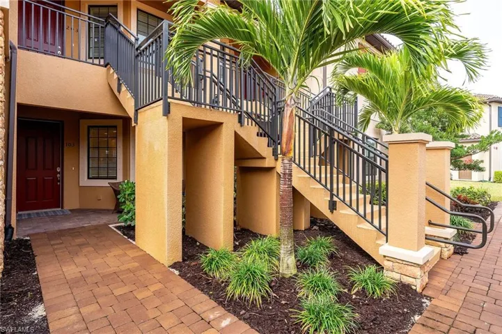 Paver walkway leading to a private entrance, exterior with stucco finish, wrought iron railings, and mature palm trees