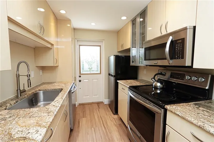 Kitchen with appliances with stainless steel finishes, light wood-type flooring, light stone countertops, and sink