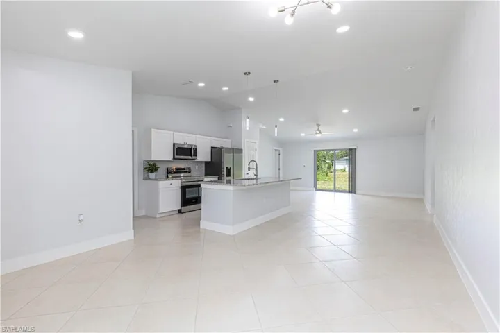 Kitchen with white cabinets, vaulted ceiling, ceiling fan with notable chandelier, stainless steel appliances, and a center island with sink