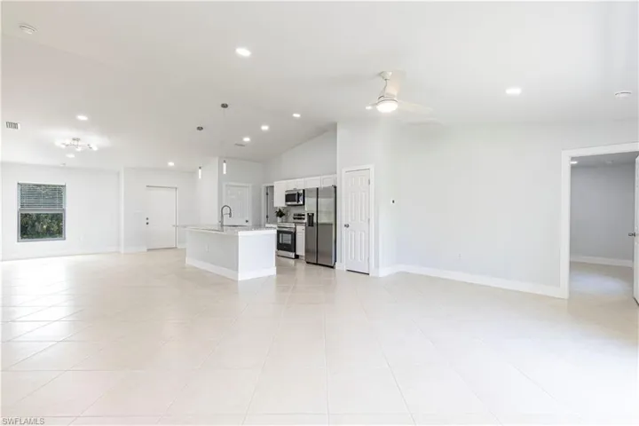 Unfurnished living room featuring ceiling fan, light tile patterned floors, sink, and vaulted ceiling