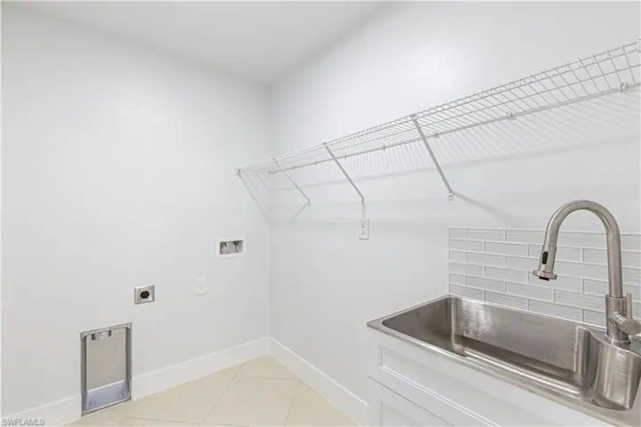 Clothes washing area featuring hookup for a washing machine, cabinets, light tile patterned floors, sink, and electric dryer hookup