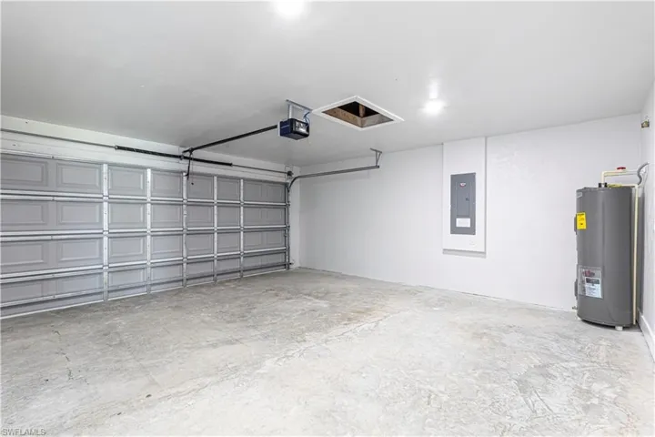 Garage featuring electric panel, electric water heater, and a garage door opener
