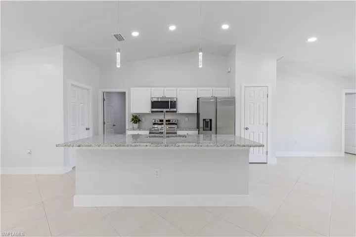 Kitchen featuring hanging light fixtures, light stone counters, stainless steel appliances, white cabinetry, and an island with sink