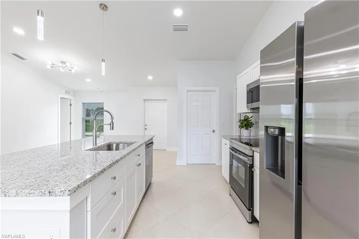 Kitchen with appliances with stainless steel finishes, an island with sink, white cabinetry, and sink