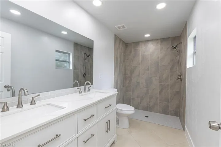 Bathroom with vanity, toilet, a healthy amount       of sunlight, and a tile shower