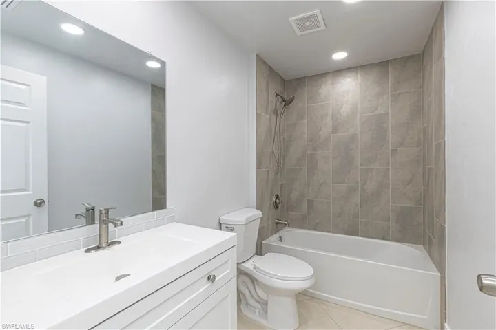 Full bathroom with tiled shower / bath combo,  vanity, toilet, and tile patterned flooring