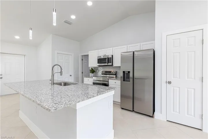 Kitchen featuring pendant lighting, sink, appliances with stainless steel finishes, a center island with sink, and white cabinets