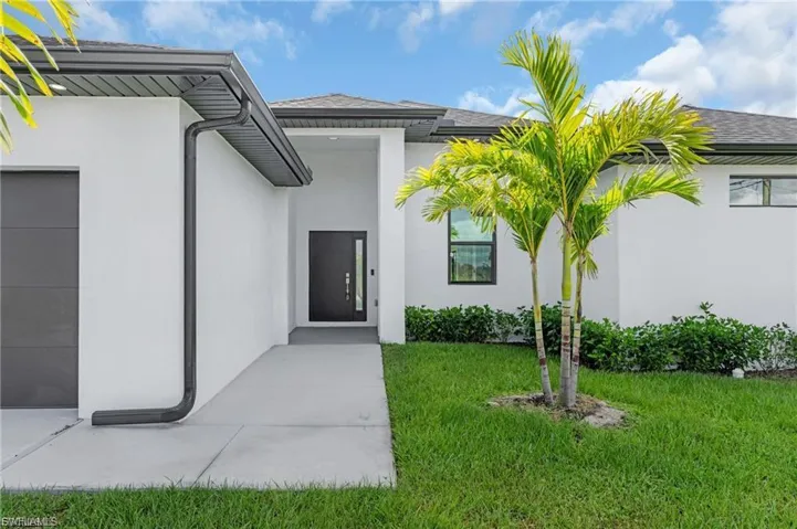 View of exterior entry featuring a garage, stucco siding, and a yard