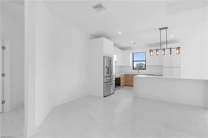 Kitchen featuring white cabinetry, stainless steel appliances, decorative light fixtures, and light stone countertops