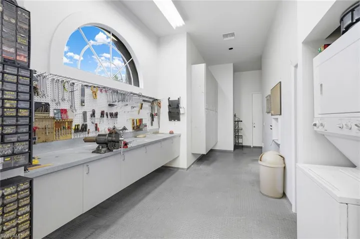 Bar featuring white cabinets, a workshop area, a high ceiling, and stacked washer / drying machine